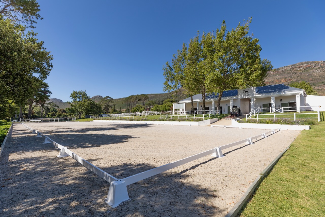 Professional dressage arena with mountain backdrop and main stable building